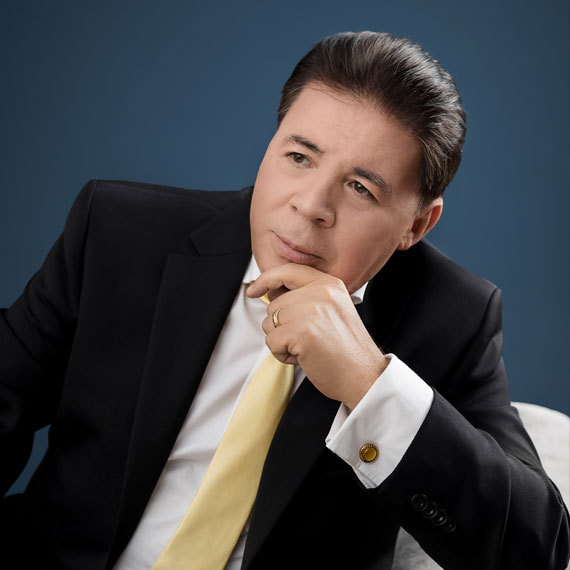 Lic. Julián Solano, sentado mirando hacia un lado, saco oscuro, camisa blanca y corbata amarilla